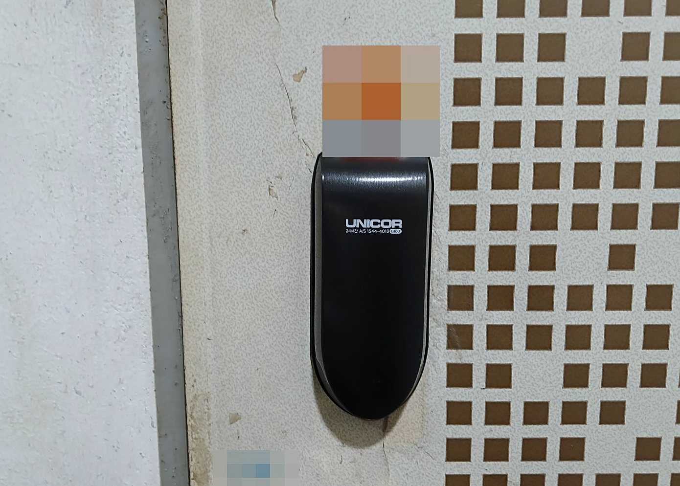 은평구 증산동 출장 — 베이지색 문에 붙은 검은 타원형 도어락 본체와 오른쪽 갈색 사각 무늬
